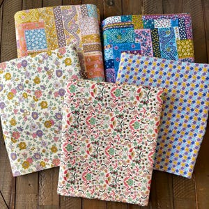 May include: A collection of folded fabric pieces with various floral and geometric patterns. The fabrics feature a mix of colors, including yellow, pink, blue, and purple. The patterns include patchwork designs, floral prints, and geometric shapes.