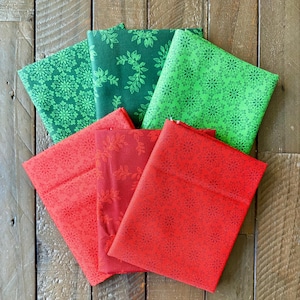 May include: A collection of folded fabric pieces in shades of green and red, each featuring a repeating floral pattern. The fabrics are arranged on a wooden surface, showcasing the various colors and designs.