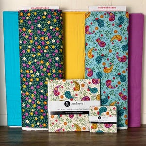 May include: A collection of colorful fabric rolls and fabric squares. The rolls include solid teal, navy floral, yellow, and paisley prints. The fabric squares are cream-colored with a paisley design. The text "#SewWithTheBest" is visible on the top of some rolls. The fabric squares are labeled "andover".