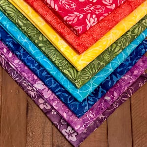 May include: A collection of colorful fabric squares arranged in a diagonal pattern. The fabrics display a variety of hues, including red, yellow, green, blue, and purple. Each square features a floral design. The arrangement creates a vibrant, rainbow-like display.