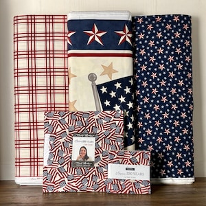 May include: A collection of patriotic fabric rolls and pre-cut squares. The fabrics feature red, white, and blue designs, including stars, flags, and plaid patterns. The pre-cut squares have the text "Anna 250 Years Deb Strain".
