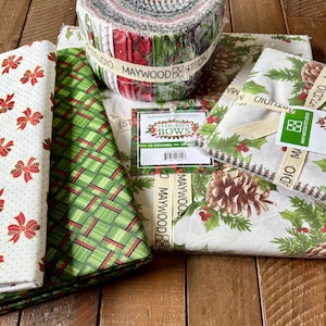 May include: A collection of Christmas-themed fabric bundles. The fabrics feature patterns of bows, pinecones, holly, and plaid in red, green, and white. The image includes a roll of fabric and several pre-cut squares, all labeled with "Maywood Studio".