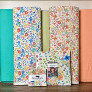 May include: Assortment of floral fabric rolls in various colors, including turquoise, green, and peach. The fabric features patterns of blue, orange, and yellow flowers. Smaller fabric squares with the text "Cannon Beach" are also visible.