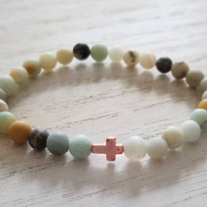 May include: A bracelet made of green, white and brown beads with a small gold cross charm.