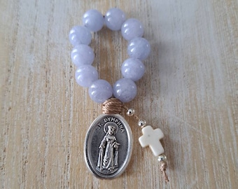 May include: A light blue gemstone rosary with a silver charm featuring a depiction of Saint Dymphna. The rosary is strung with a brown cord and includes a white cross charm.