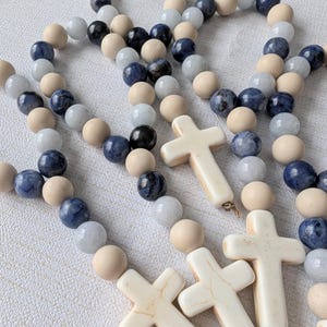 May include: A set of four beaded necklaces with wooden and blue gemstone beads and white cross charms.