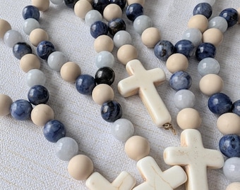 Puede incluir: Un conjunto de cuatro collares de cuentas con cuentas de madera y piedras preciosas azules y dijes de cruz blanca.