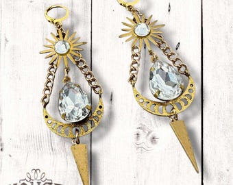 May include: Gold tone earrings with a large clear crystal, a crescent moon design, and a starburst design. The earrings are hanging from a chain.