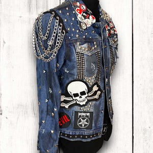 May include: A blue denim jacket with silver studs, chains, and patches. The patches include a skull and crossbones, a pentagram, and the word "EVIL".