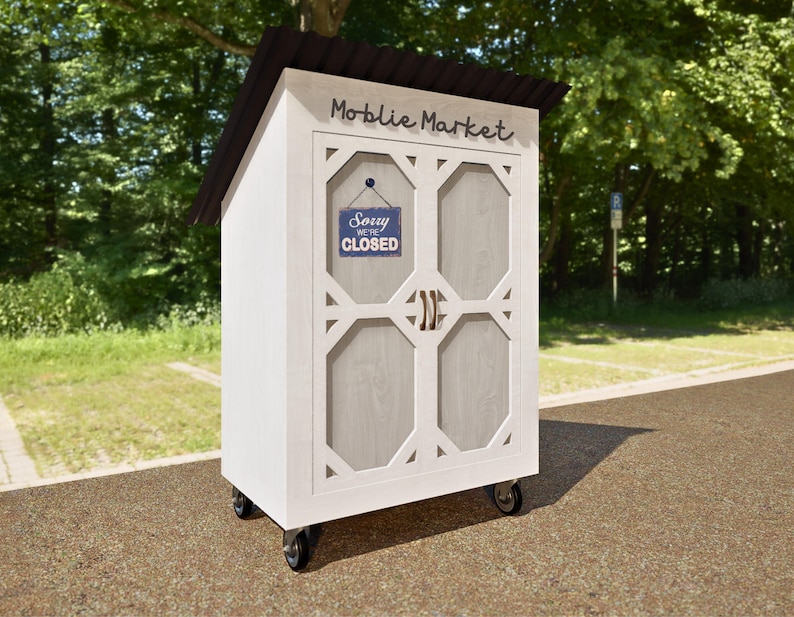 May include: A white wooden mobile market with a sign that says "Moblie Market" and a sign that says "Sorry We're Closed". The market has wheels and is in a parking lot.