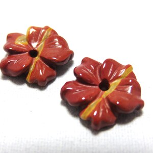 May include: Two red and yellow carved stone flower beads. The flowers have five petals and a hole in the center.