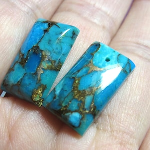 May include: Two turquoise and gold rectangular cabochons with a hole drilled through one. The cabochons have a mottled pattern of turquoise and gold.