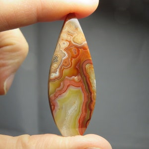 May include: A teardrop-shaped agate cabochon with a colorful pattern of red, orange, yellow, and white. The agate has a smooth, polished surface.