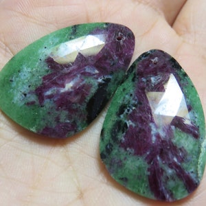 May include: Two green, purple, and black gemstone pendants with a faceted, pear-shaped design.