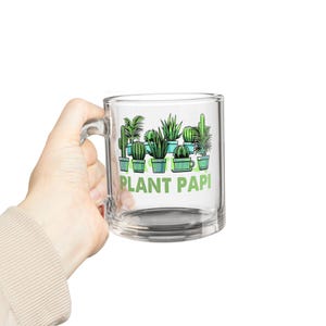 May include: A clear glass mug with a handle, featuring a green and white graphic of potted plants and the text "PLANT PAPI".