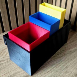 May include: A multi-tiered organiser featuring a black base and three brightly coloured trays. The trays are red, blue, and yellow, creating a striking contrast. This organiser is designed for sorting and storing items, providing a practical storage solution.