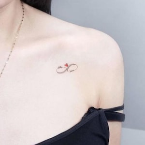 Puede incluir: Un pequeño tatuaje en forma de símbolo de infinito con los nombres "Katie" y "Joshua" escritos en su interior, con un corazón rojo en el centro.