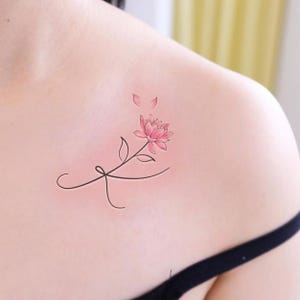 Puede incluir: Un delicado tatuaje de una flor rosa con un tallo negro delgado y hojas. La flor tiene cinco pétalos y está rodeada de tres pétalos rosas más pequeños.