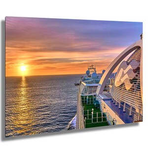 Könnte beinhalten: Ein Kreuzfahrtschiff auf dem Meer bei Sonnenuntergang. Der Himmel ist mit orangefarbenen und violetten Farbtönen gefüllt. Das Deck des Schiffes ist sichtbar, mit grünem Rasen und weißen Geländern. Das Logo des Schiffes ist oben auf dem Schiff zu sehen.