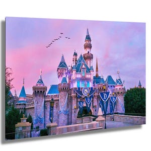 May include: A pink and purple sunset sky over Sleeping Beauty Castle at Disneyland. The castle is decorated with blue banners and a 60th anniversary sign.