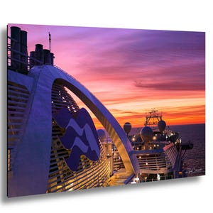 May include: A photograph of a cruise ship at sunset. The ship's structure is white and blue, with the Princess Cruises logo prominently displayed. The sky is a vibrant mix of pink, orange, and purple hues, reflecting off the ocean.