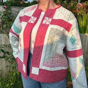 Könnte beinhalten: Eine gesteppte Jacke mit Patchwork-Muster in Rosa-, Grün- und Weißtönen. Die Jacke hat einen einfachen, offenen Frontverschluss und lange Ärmel.