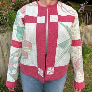 Puede incluir: Una chaqueta acolchada con un diseño de patchwork rosa y verde. La chaqueta tiene una cremallera frontal y un cuello.