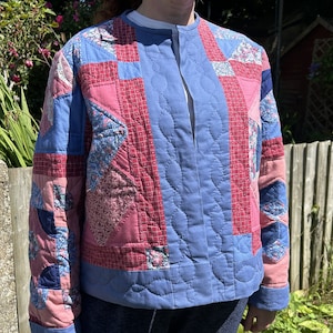 May include: A blue quilted jacket with a pink and red patchwork design. The jacket has a stand-up collar and a button closure.