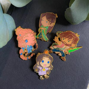 May include: Four enamel pins featuring cartoon characters. The pins depict characters in various poses and outfits, with details in shades of pink, green, blue, and brown. The pins are set against a dark background.