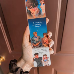 May include: A rectangular bookmark featuring illustrated characters and text. The top section shows two figures, with the text "So... are y'all like, royally betrothed or somethin?" below. The bottom section shows two more figures with the text "What! No, no, no! We are just friends who happen to train together at the castle!!"