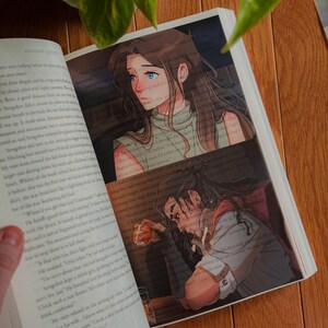 May include: Open book with illustrations. One illustration shows a woman with long brown hair and blue eyes. The other illustration shows a man with long dark hair. The book is open on a wooden surface.