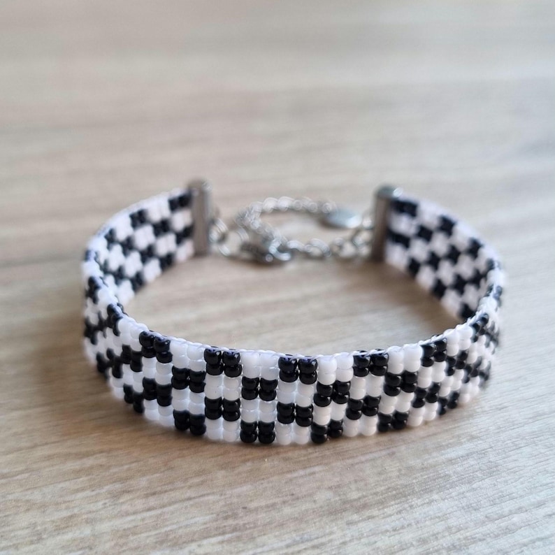 Puede incluir: Un brazalete de cuentas de color blanco y negro con un cierre plateado.