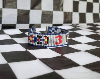 May include: A beaded bracelet with a blue, grey, red and yellow pattern. The bracelet has a silver clasp.