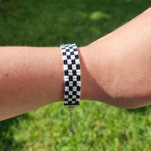 Puede incluir: Un brazalete de cuentas de color negro y blanco con un dise&ntilde;o de tablero de ajedrez y un cierre plateado.