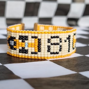 Puede incluir: Una pulsera de cuentas amarillas y negras con la palabra "GLOW" escrita en cuentas negras.