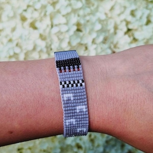 Peut inclure: Un bracelet gris en perles avec un motif à carreaux noir et blanc et des accents rouges.