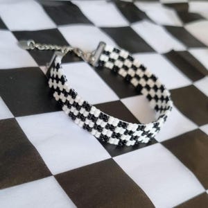 Puede incluir: Un brazalete de cuentas de color blanco y negro con un cierre plateado.