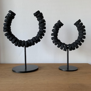 Könnte beinhalten: Zwei schwarze dekorative Skulpturen. Jede Skulptur hat ein halbkreisförmiges Design aus gestapeltem, strukturiertem Material. Die Skulpturen sind auf dünnen, schwarzen Metallständern mit runden Basen montiert. Der Hintergrund ist eine hellfarbige Wand.