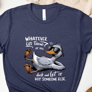 May include: Heather navy t-shirt with a graphic of a relaxed duck wearing sunglasses. The text reads "WHATEVER LIFE THROWS at you, duck and let it HIT SOMEONE ELSE."