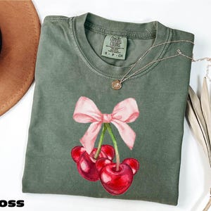 a green shirt with a pink bow and cherries on it