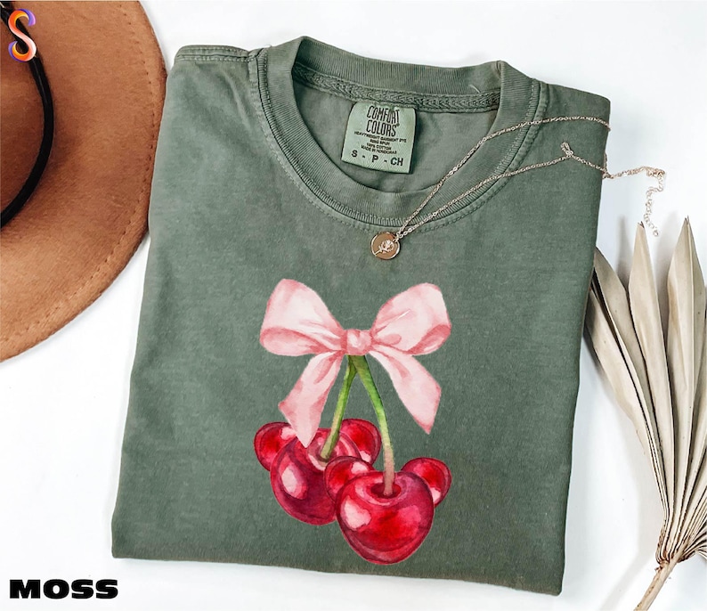 a green shirt with a pink bow and cherries on it
