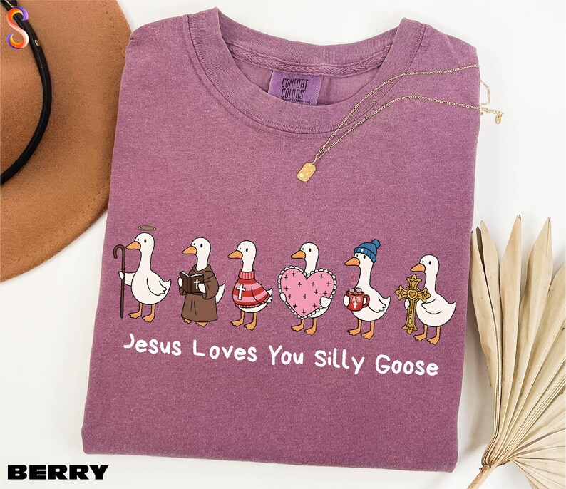 A purple t-shirt with a graphic design of six cartoon ducks, each with a different outfit or accessory, and the text "Jesus Loves You Silly Goose" printed on it.