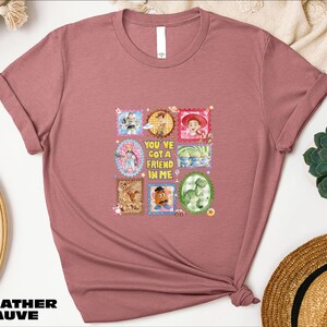 a pink t-shirt with a graphic design of various cartoon characters and a message that says "You'll Got a Friend in Me".
