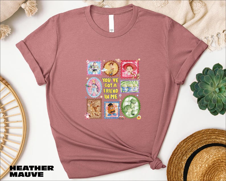 a pink t-shirt with a graphic design of various cartoon characters and a message that says "You'll Got a Friend in Me".