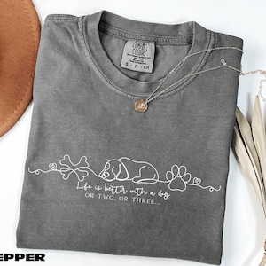 a gray t-shirt with a white design, a necklace, a hat, and some dried leaves, all arranged on a white surface.