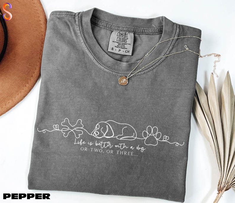 a gray t-shirt with a white design, a necklace, a hat, and some dried leaves, all arranged on a white surface.