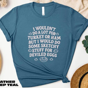 A blue t-shirt with a humorous text printed on it, along with some other items such as a hat and a plant.