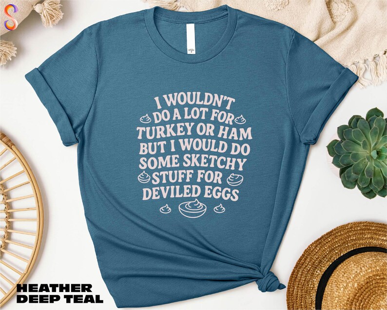 A blue t-shirt with a humorous text printed on it, along with some other items such as a hat and a plant.