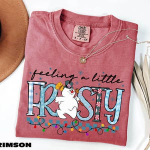 A red t-shirt with a cartoon snowman and the text "feeling a little FROSTY" printed on it, along with a necklace and a hat.