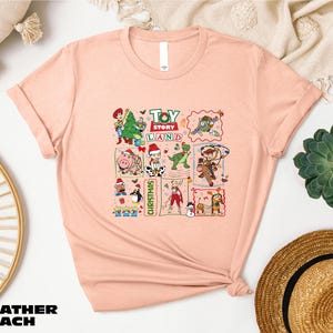 a pink t-shirt with a cartoon-style design of various characters from the Toy Story franchise, including Woody, Buzz Lightyear, and other beloved characters from the Toy Story movies. The t-shirt is displayed on a white background, surrounded by various accessories such as a straw hat, a woven basket, and a potted plant.